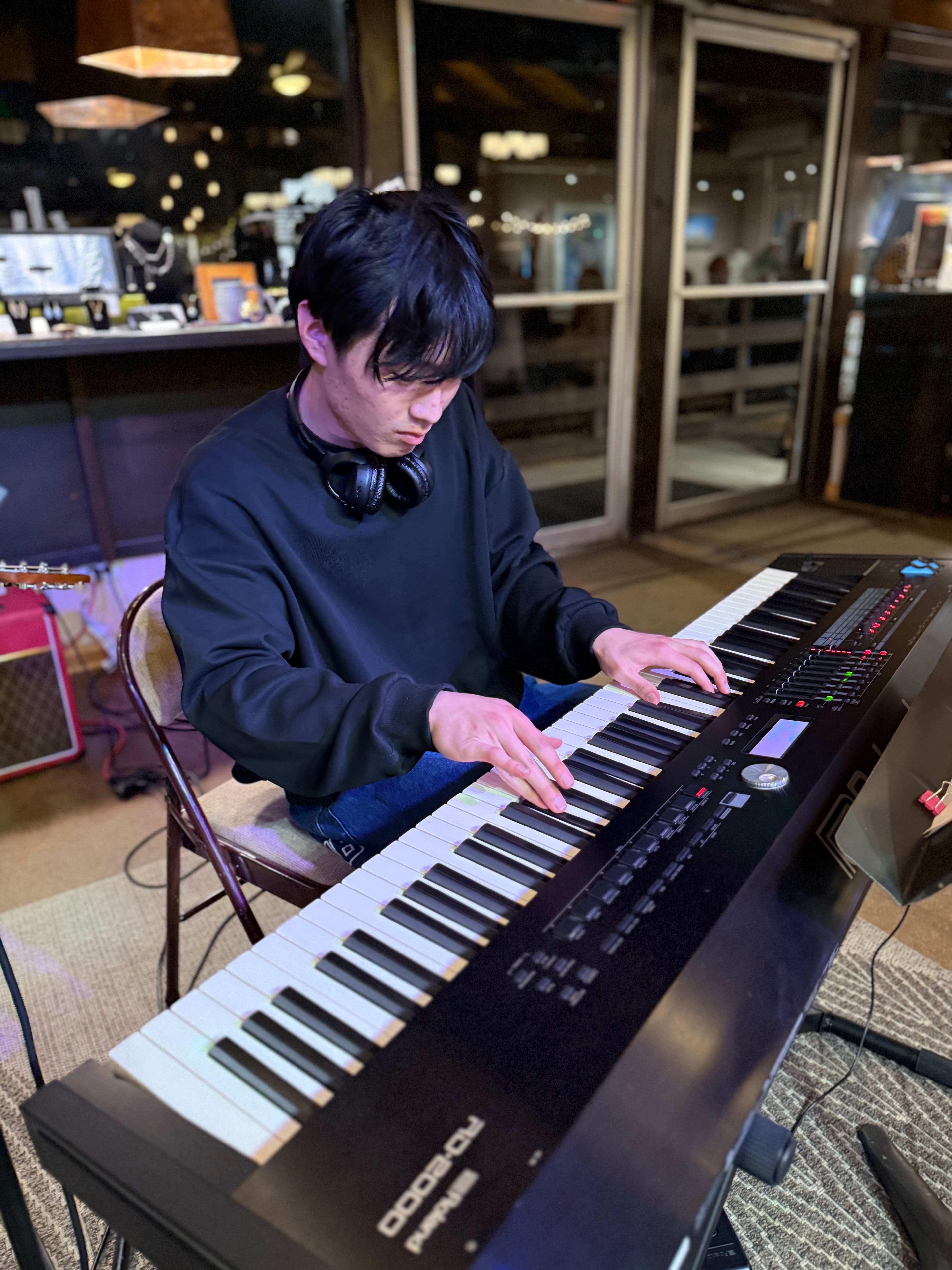 Young man playing a digital keyboard in a dimly lit indoor space at night.