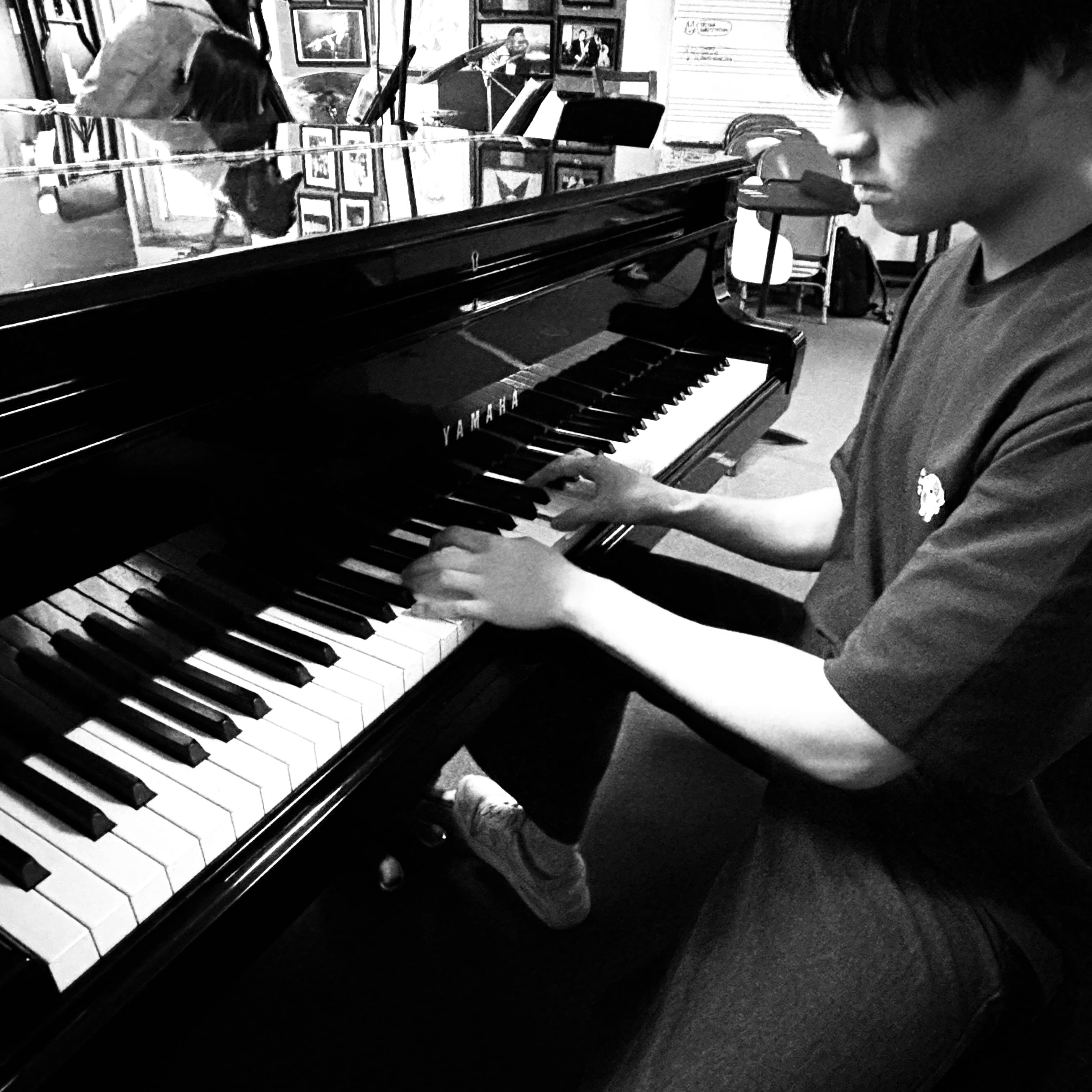 Focused young man playing a black Yamaha grand piano in a black and white photo.